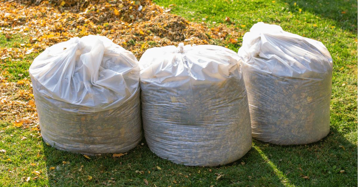 three bags of yard waste in front of a pile of leaves
